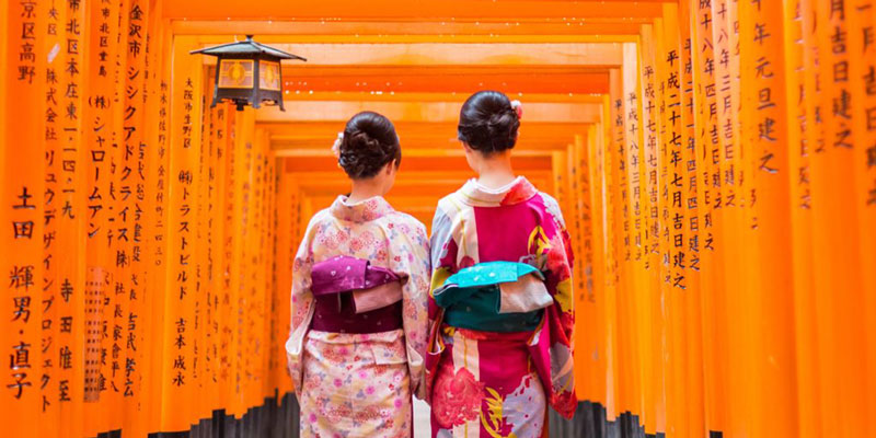 Two geishas among red wooden Tori Gate at Fushimi Inari Shrine in Kyoto Japan