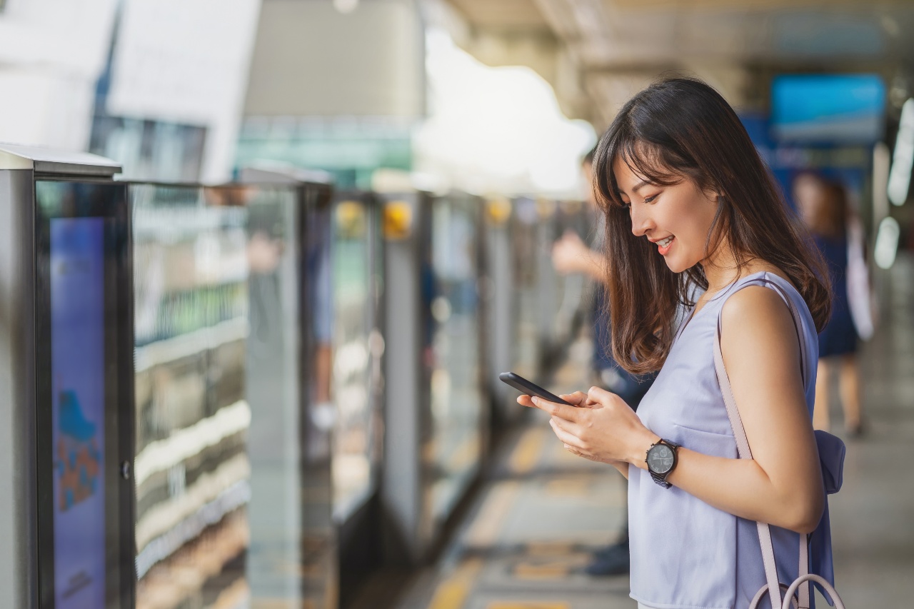 Japanese woman at platform using phone and watching social media advertising in Japan